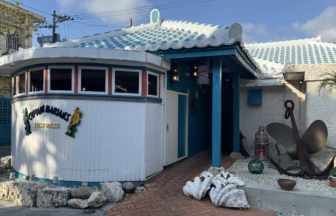 Seafront restaurant with a curved white exterior, turquoise trim, and a blue tiled roof, sea-themed decor on the façade.